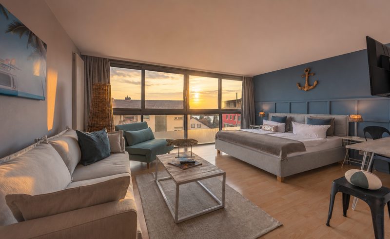 Zimmer im Ko'Ono mit Sofa, Doppelbett und Panoramafenster im Abendlicht